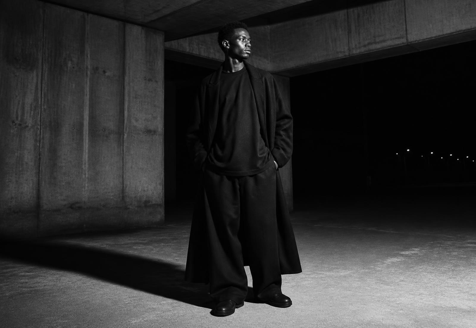 Model in an oversized coat and wide trousers in a concrete underpass